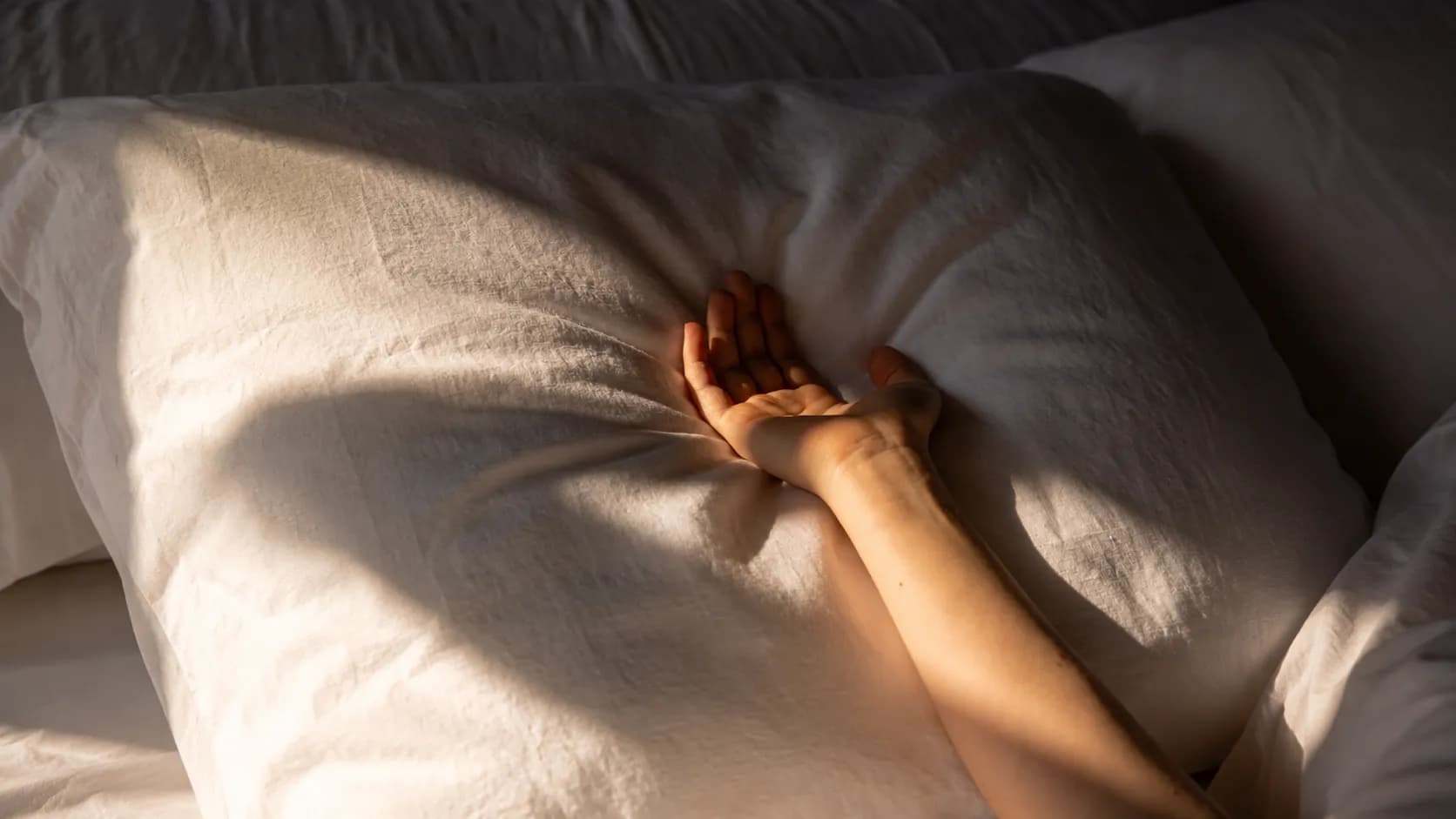 A close-up of arms resting on a pillow, warm sunlight falling across the bed.
