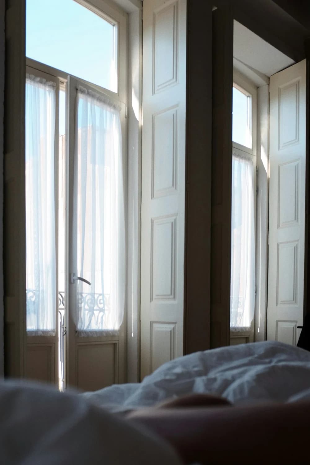 Soft morning light through French doors above a rumpled bed.