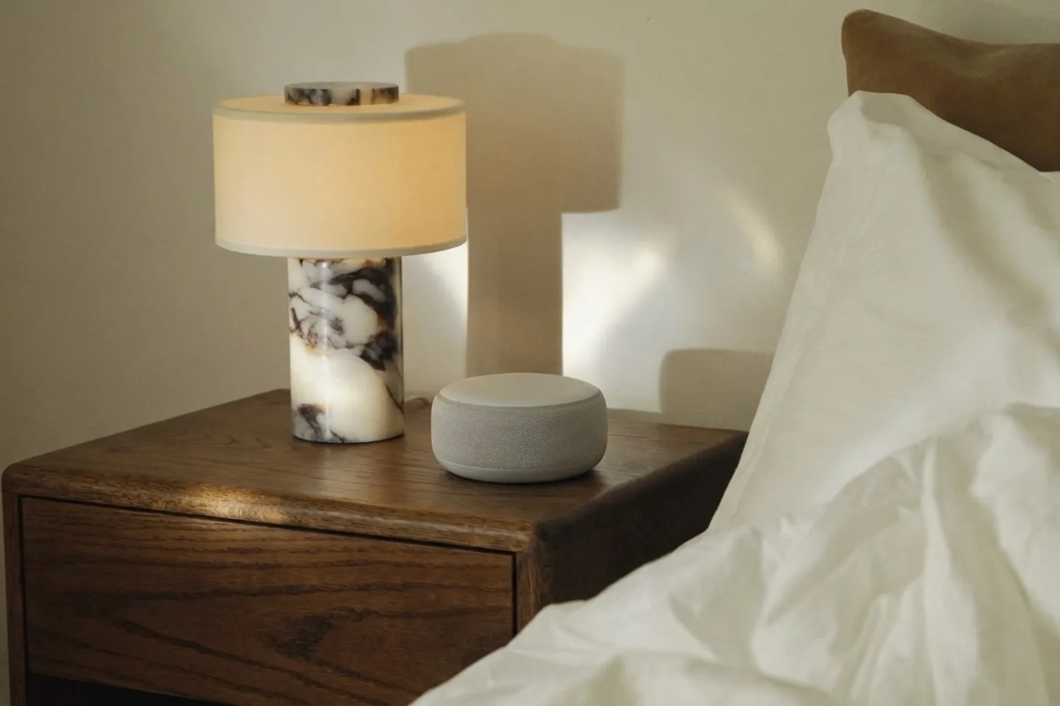 A Wove sensor on a nightstand beside a lit bedside lamp at dusk.